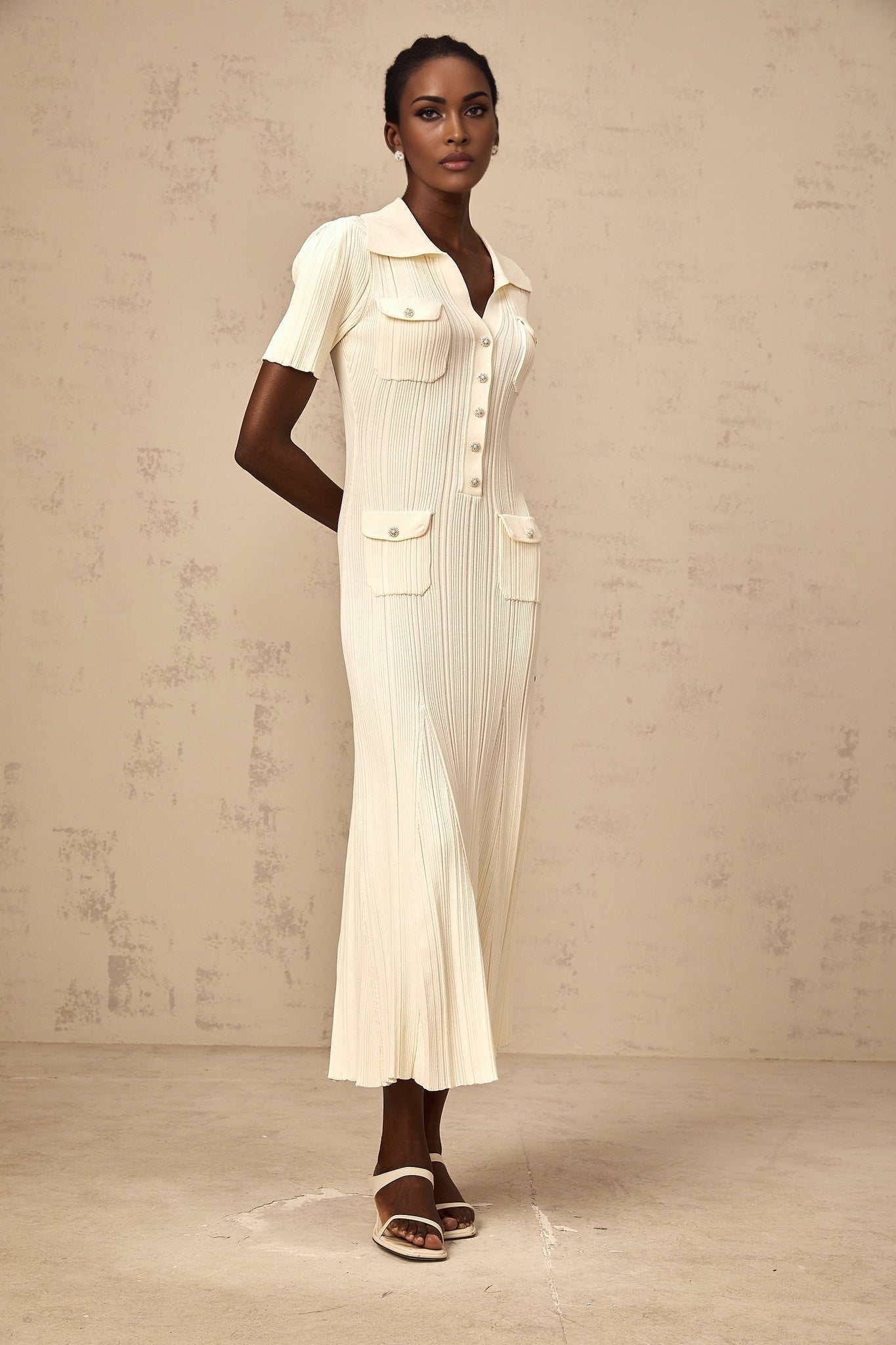A woman wearing a formfitting ribbed knit midi dress in a neutral color standing in a relaxed pose