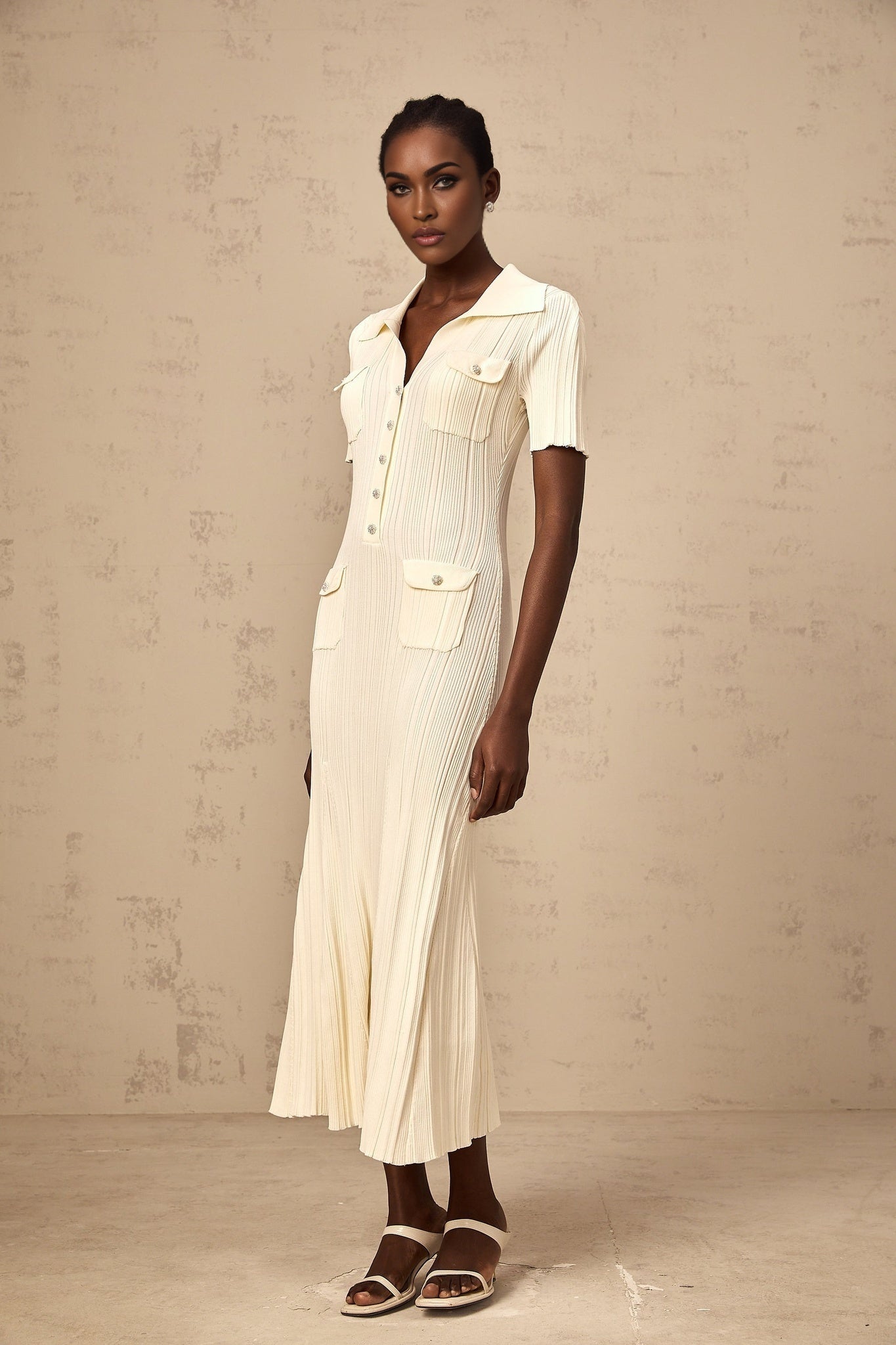 Woman wearing a beige ribbedknit midi dress with long sleeves and a formfitting silhouette standing against a plain background