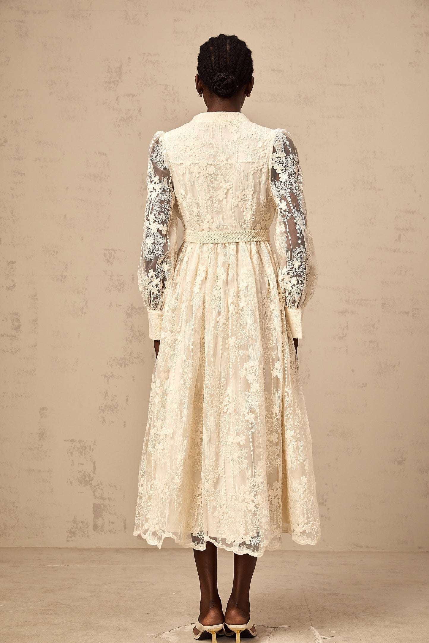 Woman wearing a neutral colored midi dress with lace embroidery details and a flowy silhouette