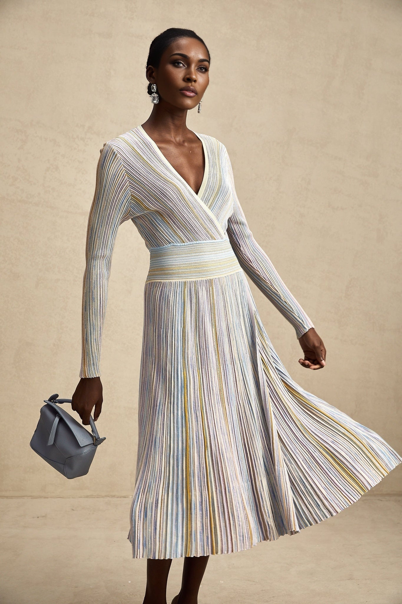 A woman wearing a long knitted midi dress with vertical stripes standing in a casual pose