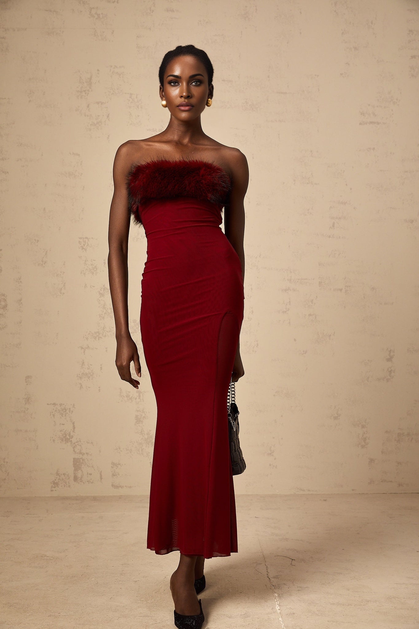A woman wearing a red faux fur off shoulder midi dress with mesh details standing against a plain background