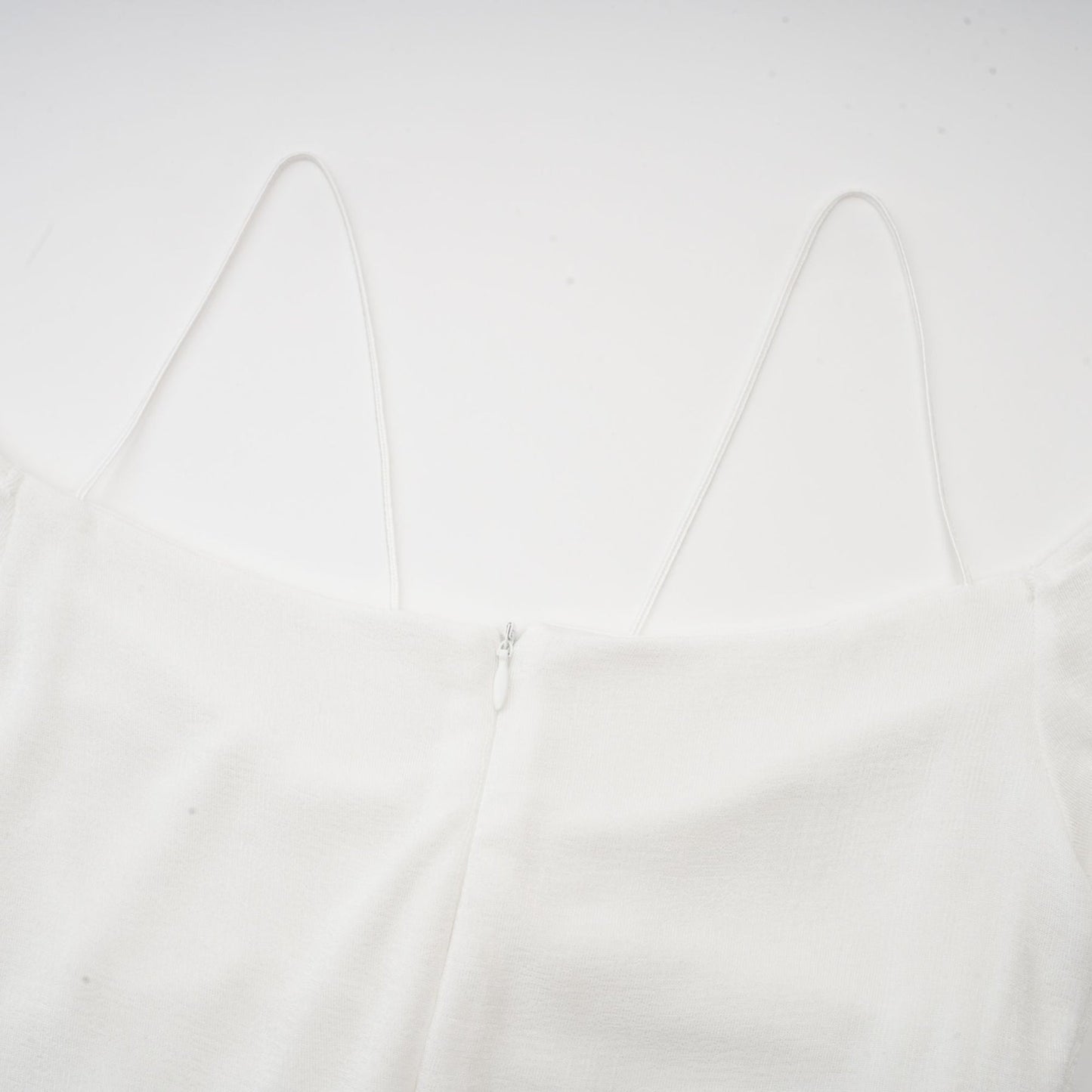 A white offshoulder maxi dress with panel detailing worn by a model standing against a plain background