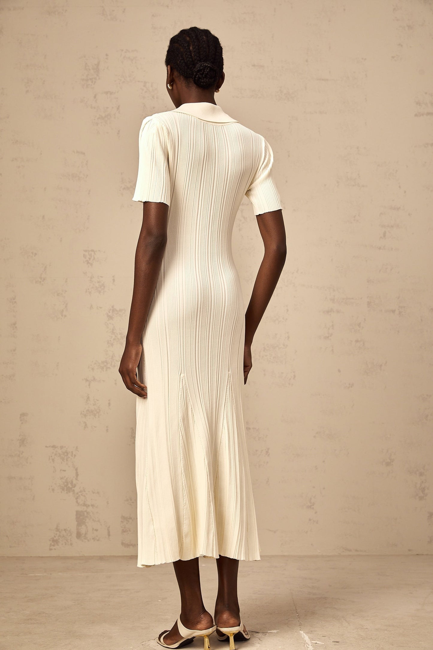 A woman wearing a neutralcolored ribbed knit midi dress with a formfitting silhouette standing against a plain background