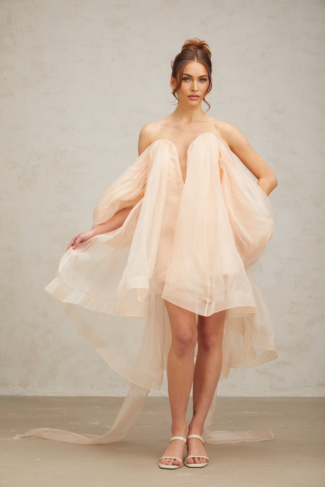 Woman wearing a short flowy dress with a large bow detail and voluminous sleeves in a pastel color