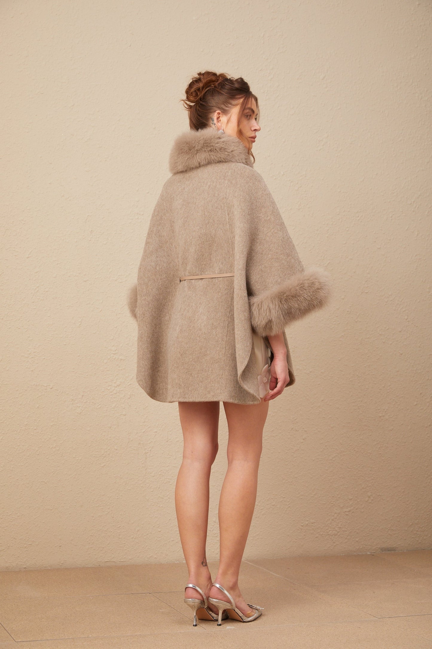 Woman wearing a brown wool cape coat with fur trim and belt fastened at the waist