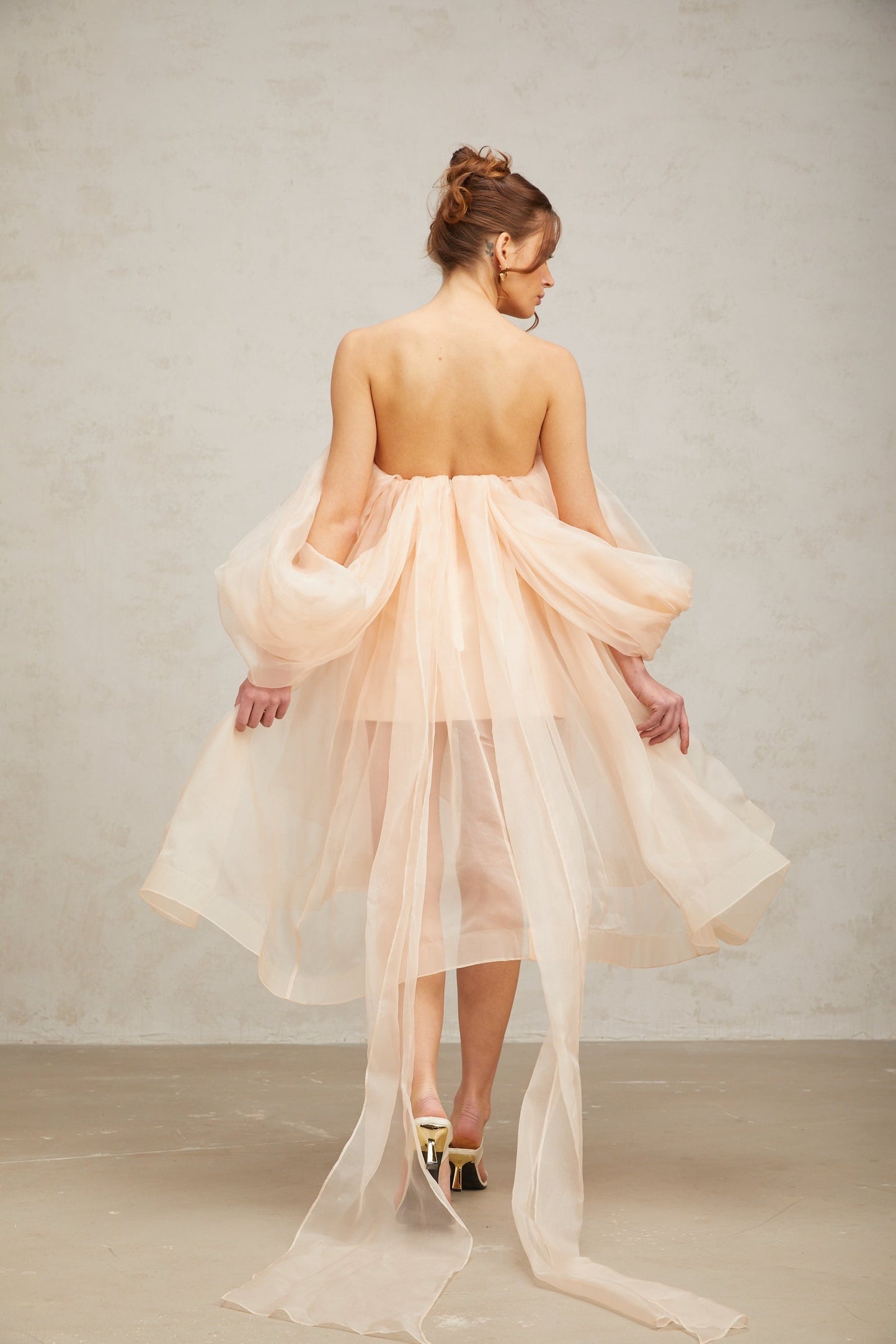 A short pink mini dress with puffy sleeves and a large bow detail at the front featuring a voluminous silhouette
