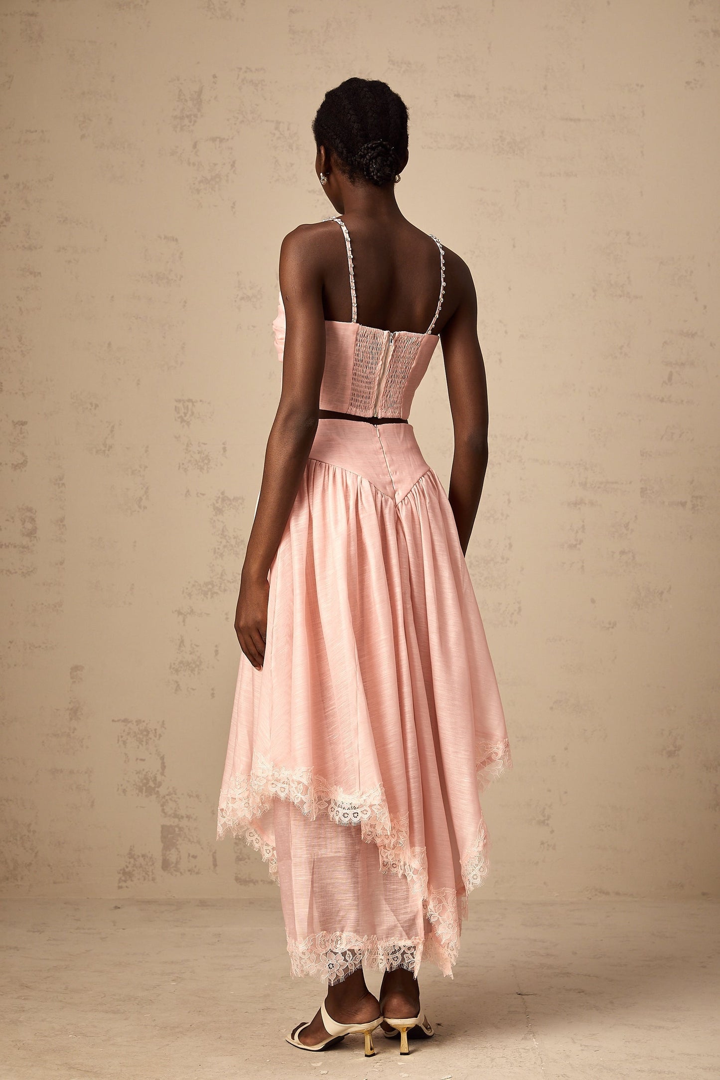 A woman wearing a pink matching set consisting of an asymmetric ruffled top and skirt The top has one shoulder and the skirt features a ruffle detail The outfit is vibrant and feminine