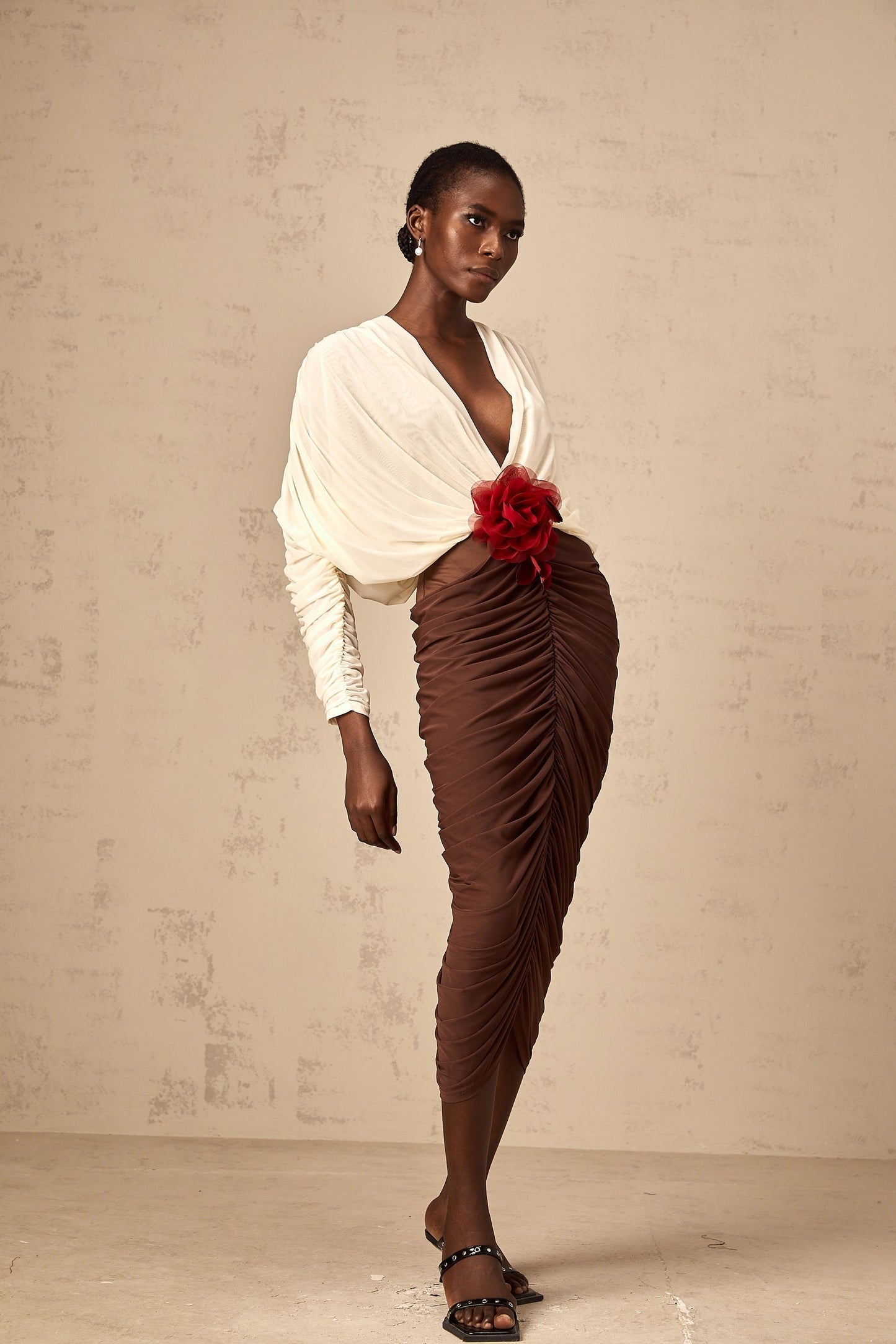 A woman wearing a colorblocked midi dress with a ruched design and a large flower brooch accent The dress features contrasting colors and falls to mid calf length