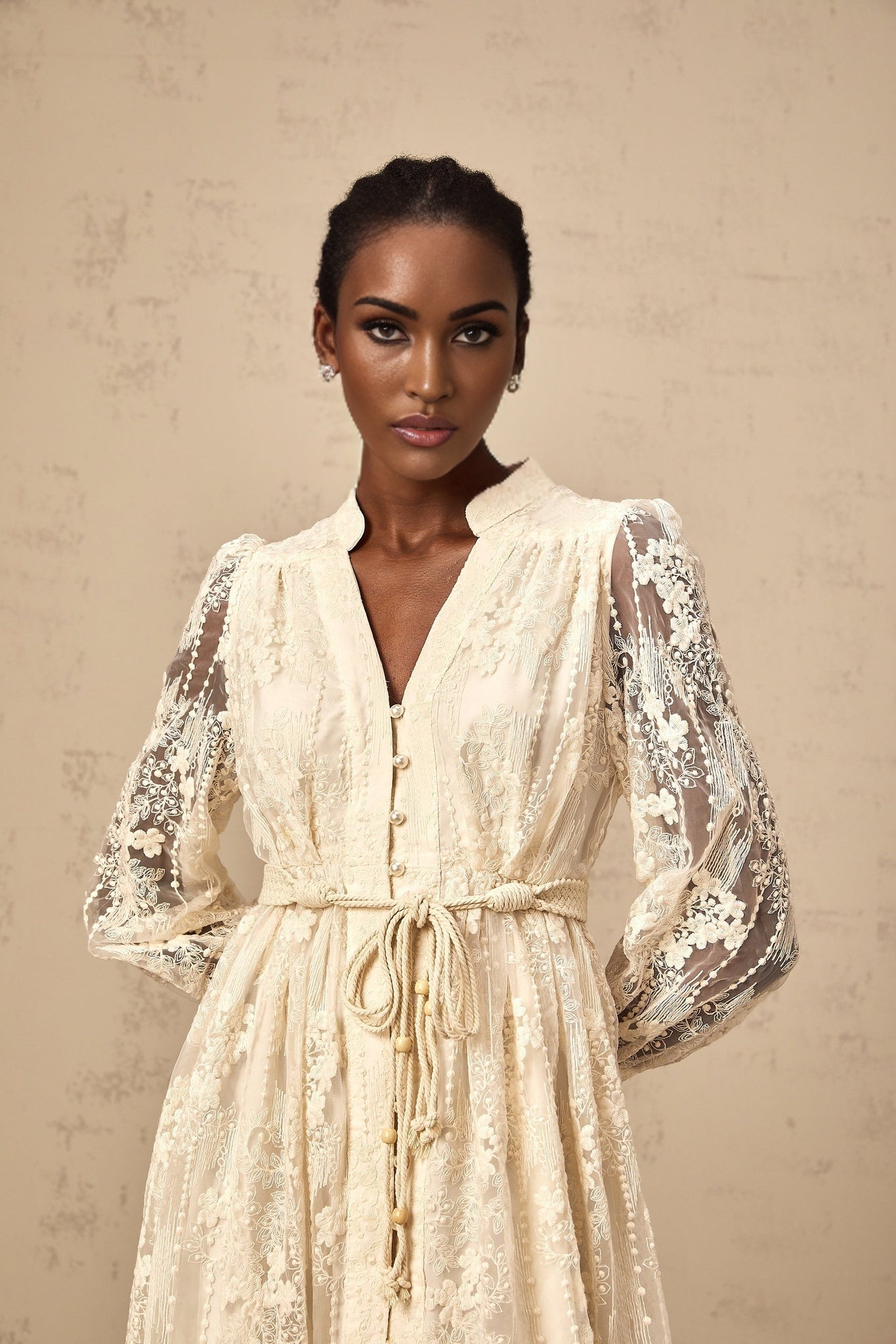 Woman wearing a neutral colored midi dress with lace embroidery details standing in a relaxed pose