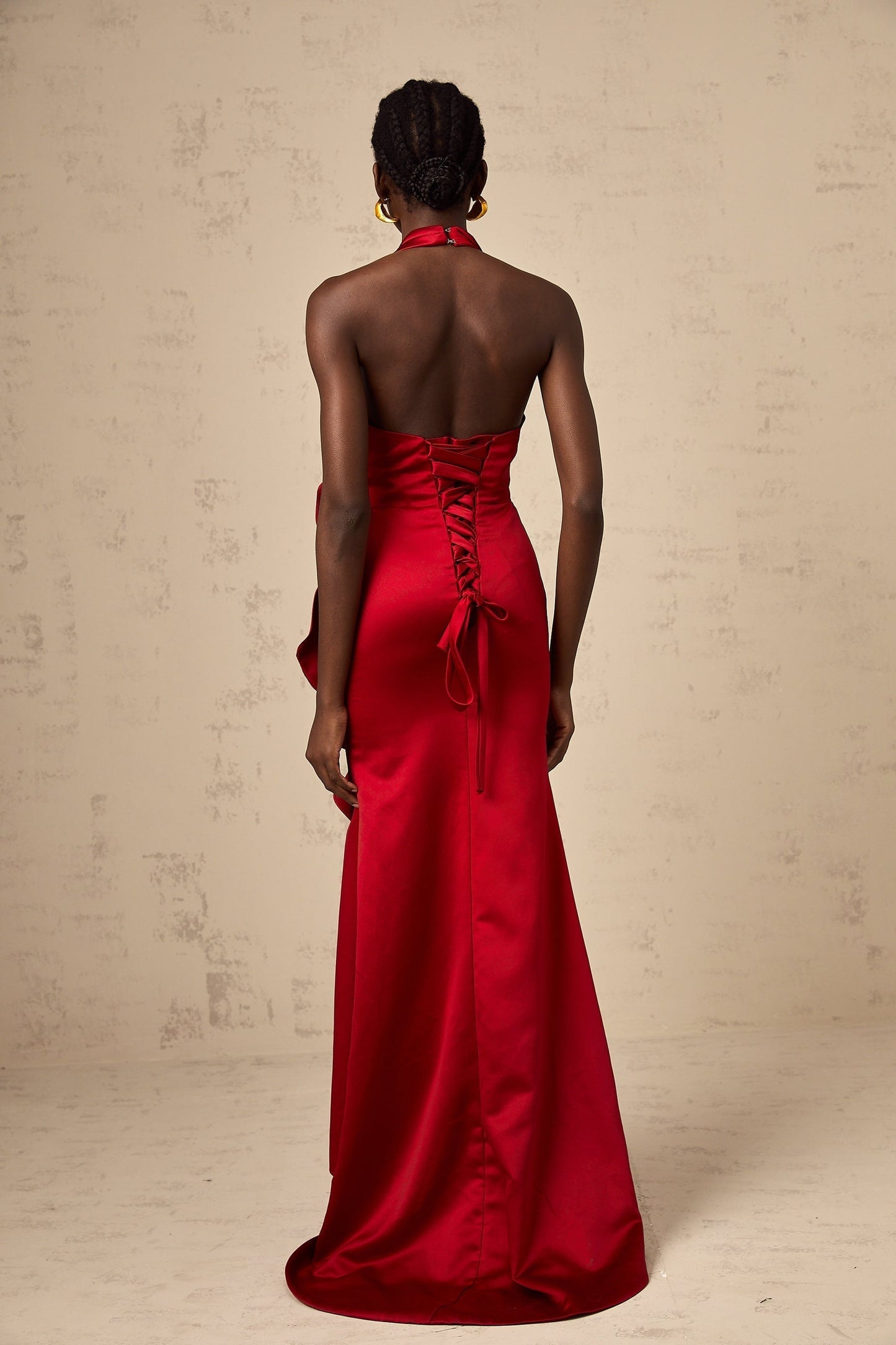 A woman wearing a vibrant red halterneck maxi dress with ruffled 3D petal details cascading down the length of the gown creating a dramatic and elegant silhouette