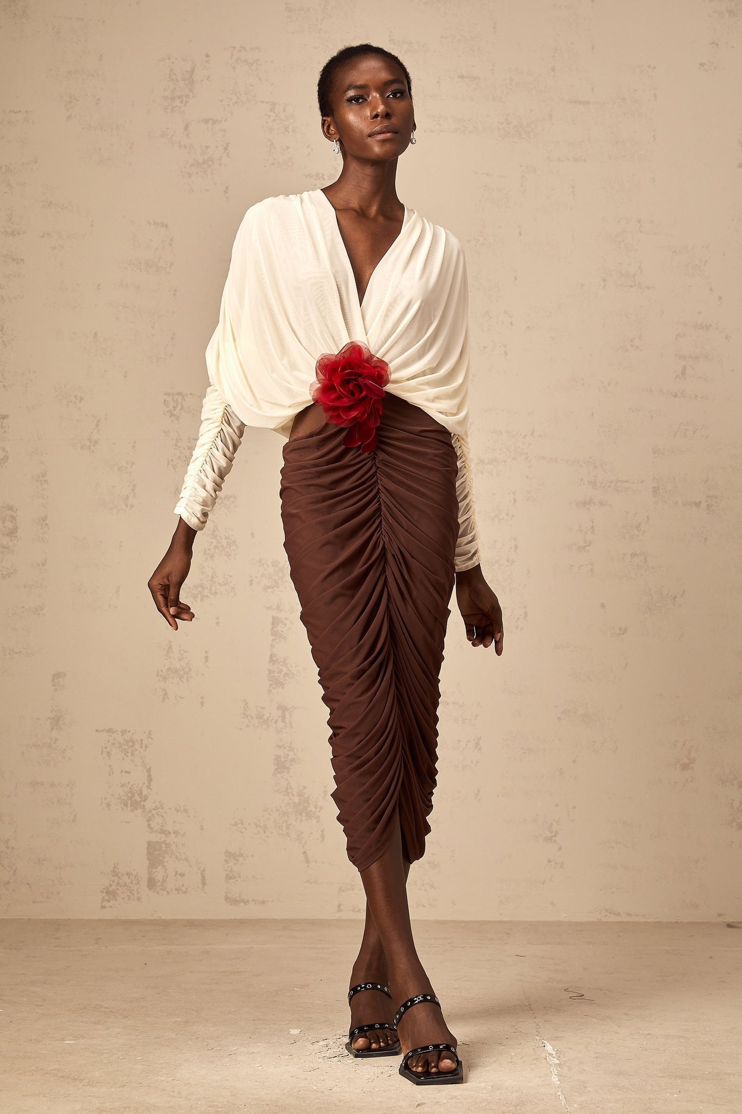 A midi dress with color blocking and ruching featuring a flower brooch The dress is named Leontine and has a mid length design