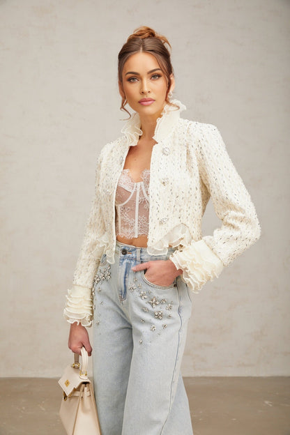 A white cropped jacket with beaded details and ruffle trim on a plain background