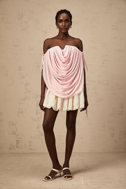 A pink offshoulder ruched top with a gathered fabric design worn by a model against a plain background