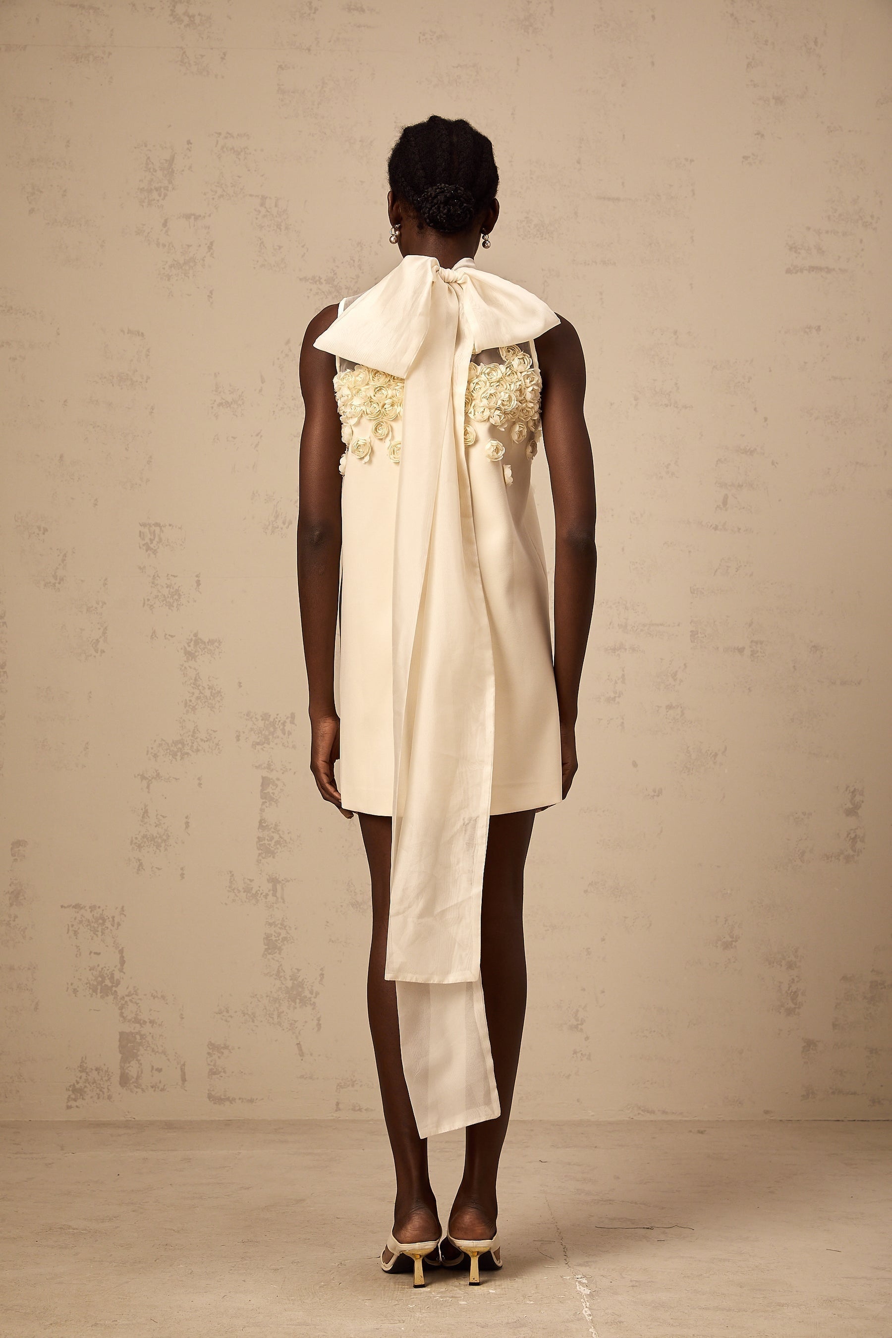 A sleeveless mini dress with faux flower details in a light color against a plain background