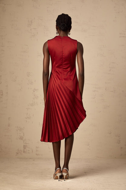 A woman wearing a wine red midi dress with an asymmetric neckline and pleated skirt standing against a plain background