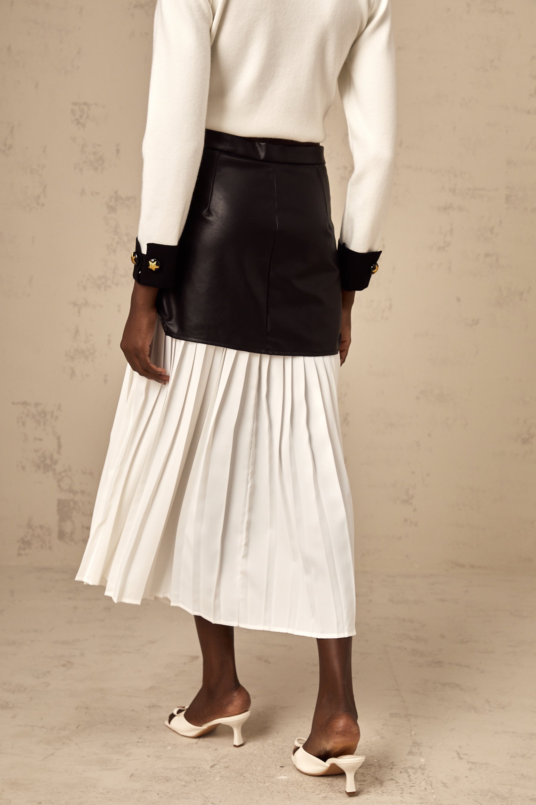 Woman wearing a colorblocked midi skirt with pleated panels in contrasting colors standing against a plain background