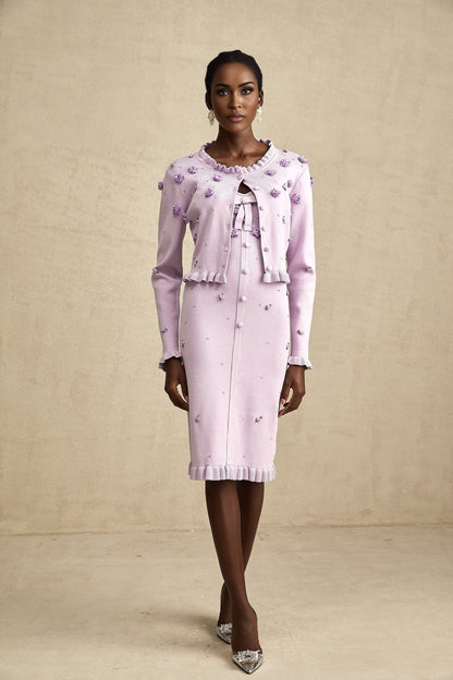 Woman wearing a purple knitted cardigan over a matching dress with faux flower embellishments on both pieces