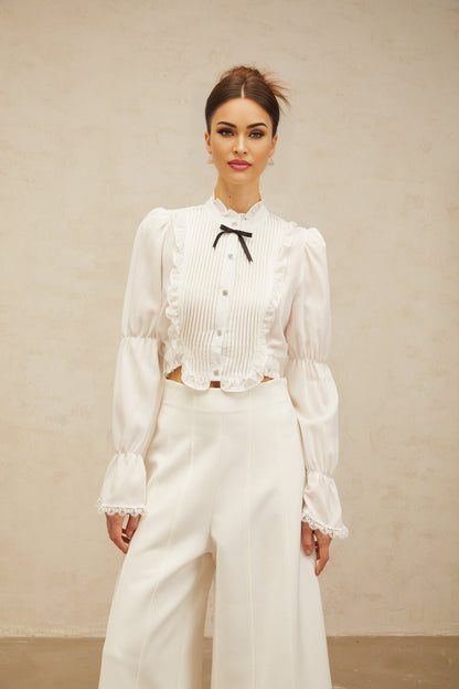 A white ruffled shirt with a bowknot detail and shirred panels featuring a feminine and elegant design