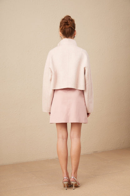 Woman wearing a pink short coat with diagonal placket closure standing against neutral background