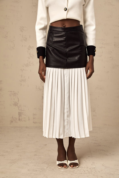 Woman wearing a colorblocked pleated midi skirt with contrasting panels in multiple colors standing in a neutral background