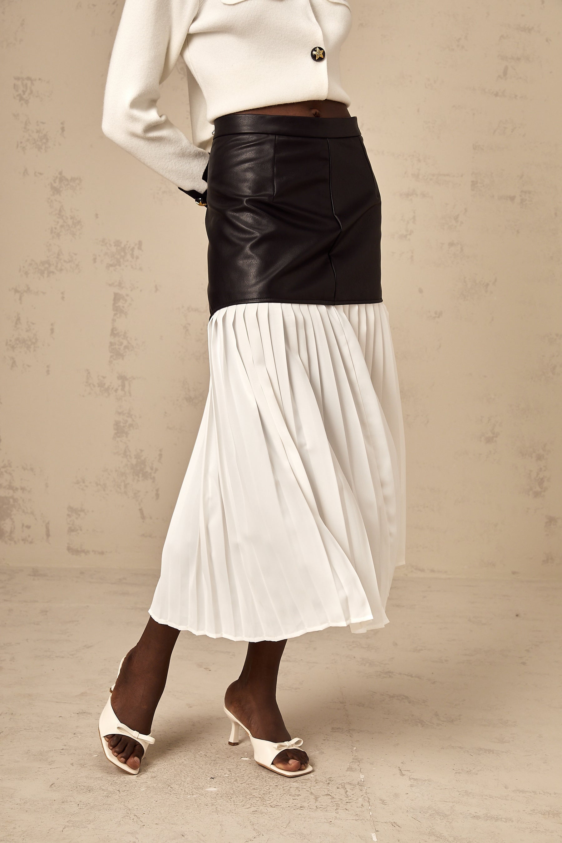 Woman wearing colorblocked pleated midi skirt with contrasting panels in different shades standing against plain background
