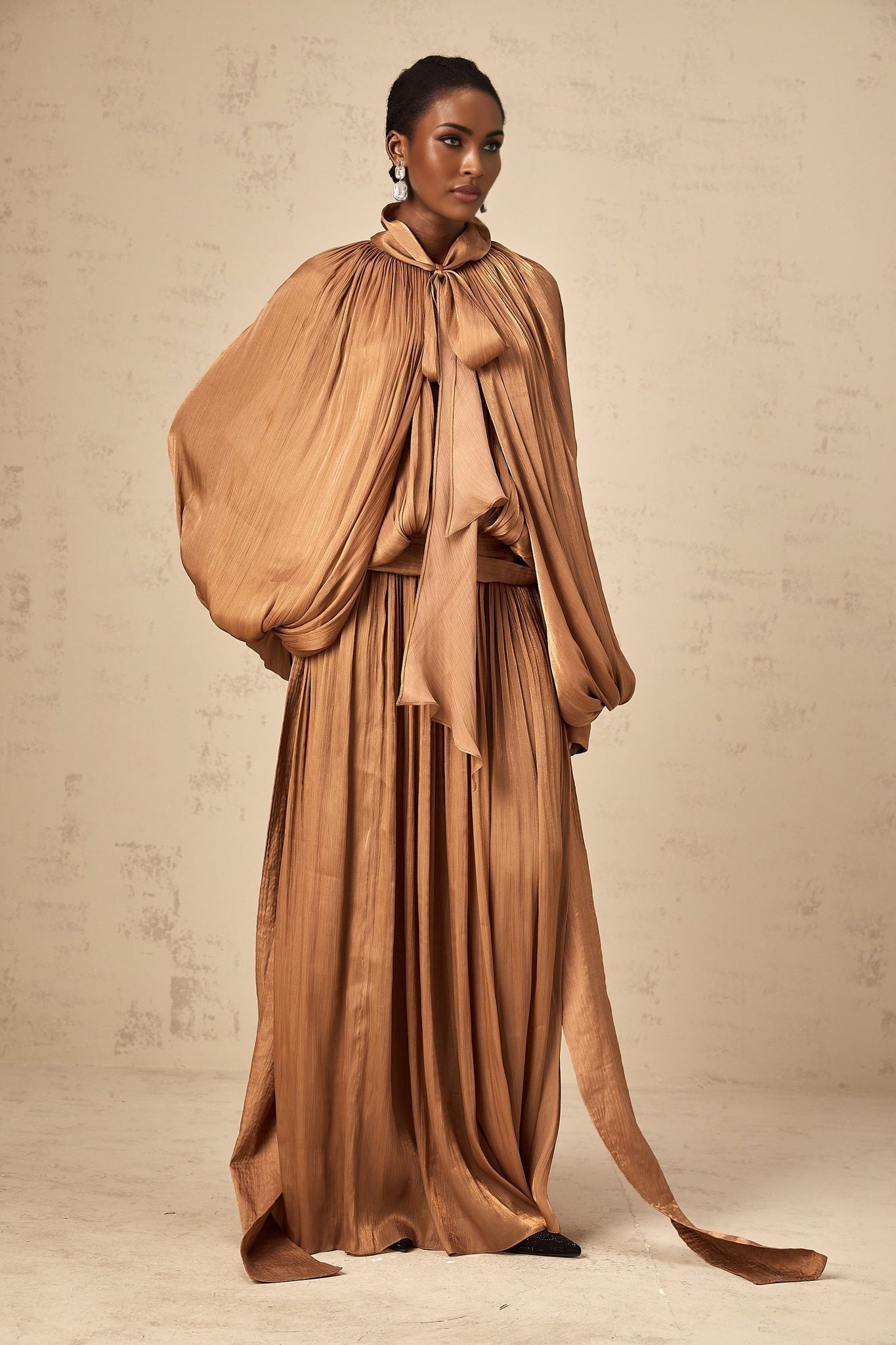 Woman wearing long brown pleated satin maxi dress with flowing skirt and sleeveless design