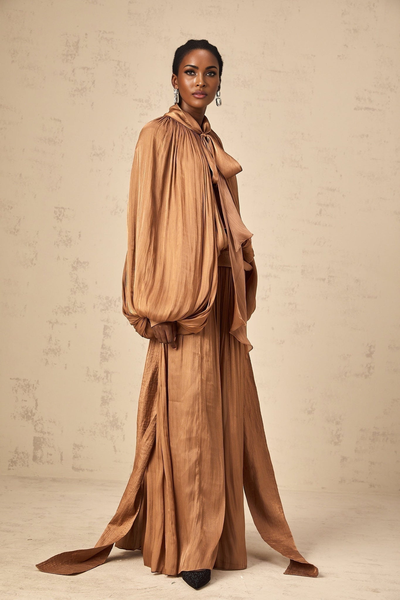Woman wearing long brown pleated satin maxi dress with flowy skirt and fitted bodice