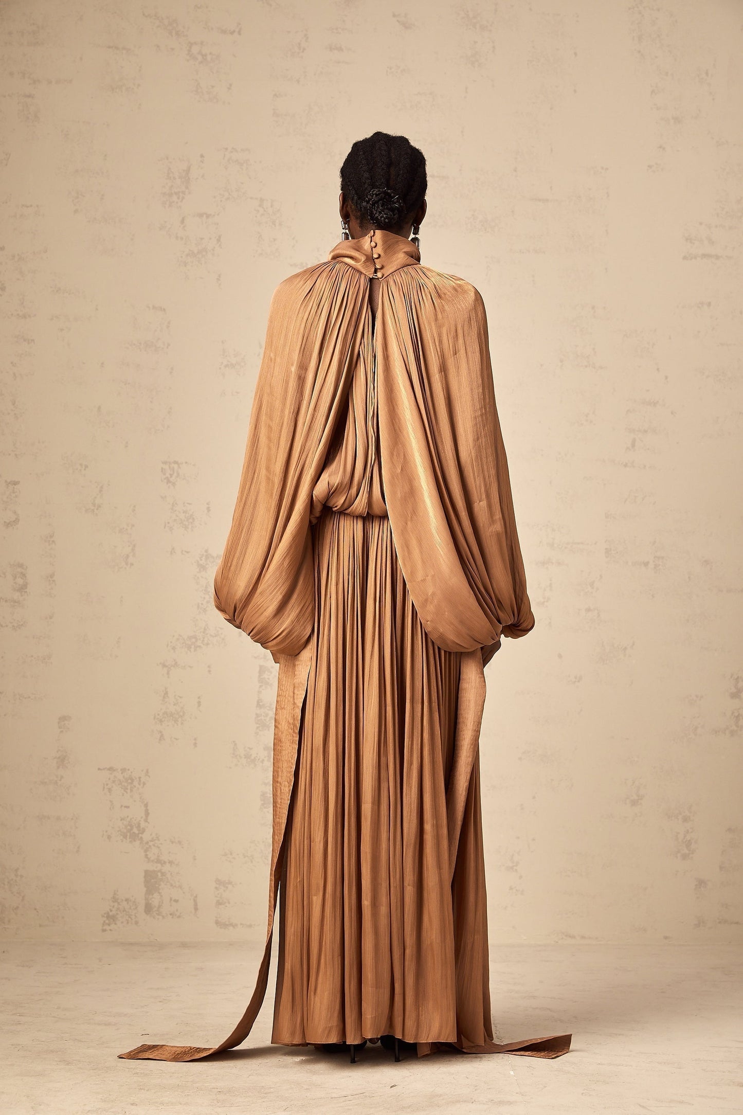 A long brown satin maxi dress with pleated details and a flowing silhouette