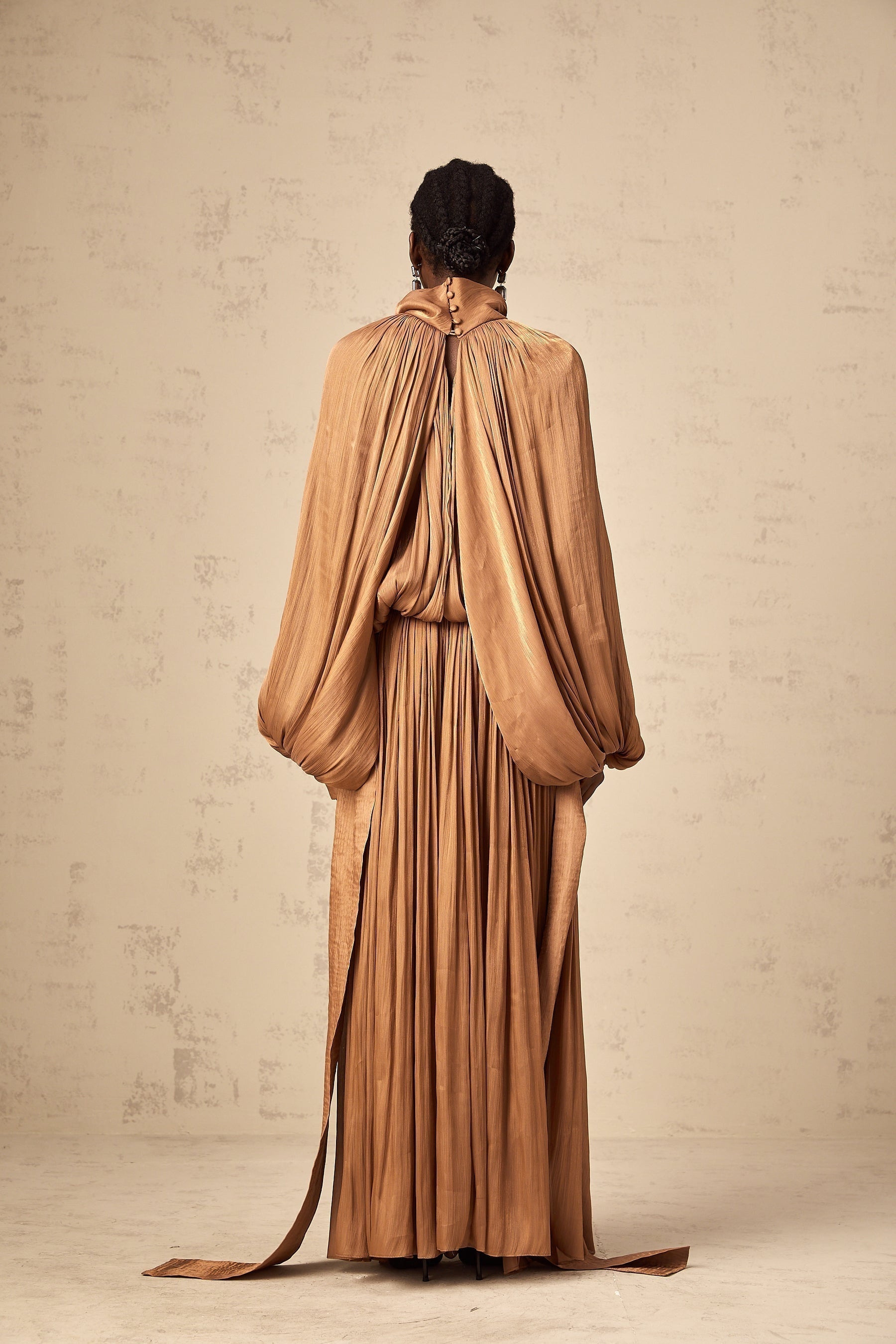 A long brown satin maxi dress with pleated details and a flowing silhouette
