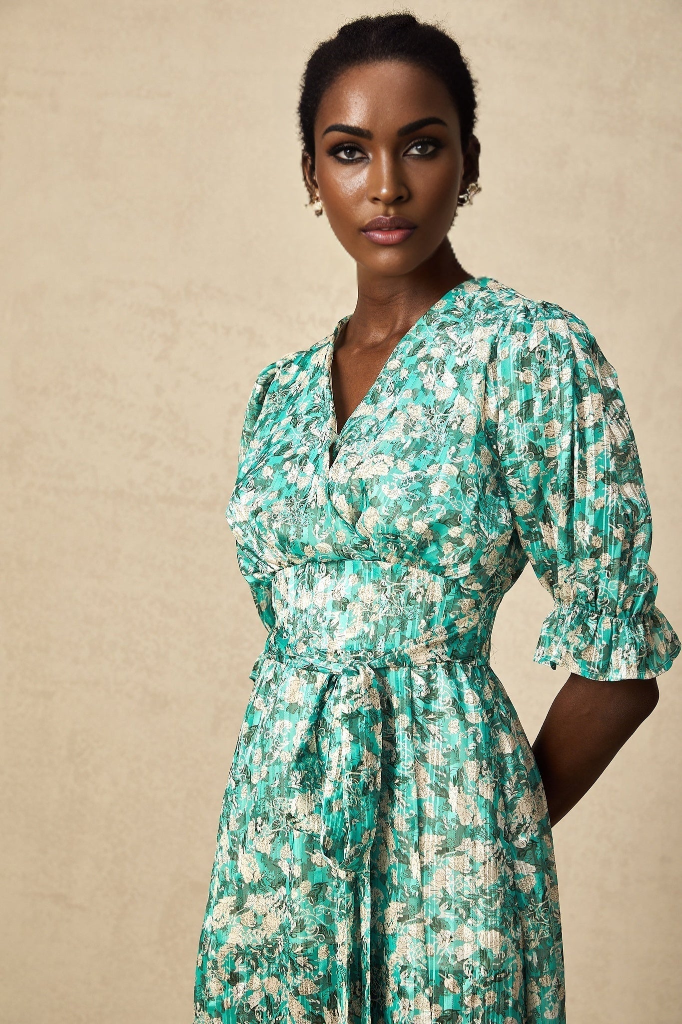 Woman wearing green midi dress with floral print and high slit standing against plain background