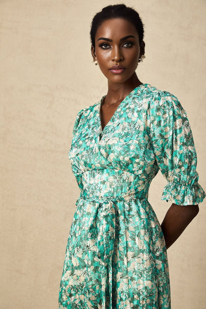 Woman wearing green midi dress with floral print and high slit standing against plain background