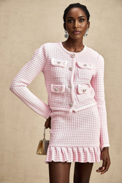 Young woman wearing a pink waffle knit jacket and matching skirt set standing against a plain background