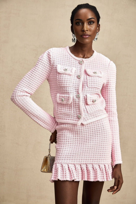 Young woman wearing a pink waffle knit jacket and matching skirt set standing against a plain background