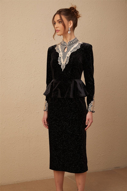 A woman wearing a black velvet midi dress with embellishments standing in a neutral pose against a plain background