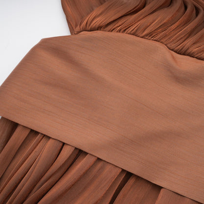 Woman wearing long brown pleated satin maxi dress with flowy skirt and fitted bodice