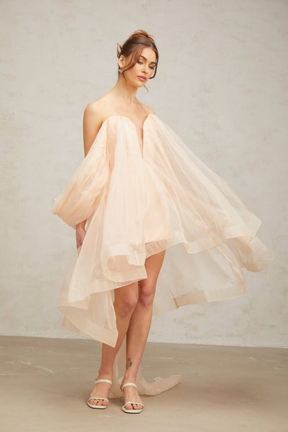 Young woman wearing a short puffy mini dress with large bow detail at the waist and voluminous skirt in a light color