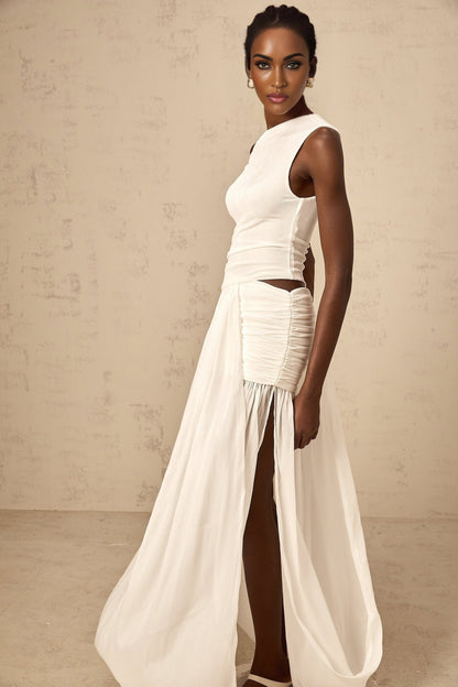 Woman wearing long white dress with one shoulder strap and gathered fabric details flowing to floor length