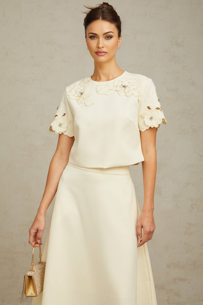 A woman wearing a neutralcolored matching set consisting of a top and skirt The top features delicate 3D petal details and the skirt has a fitted silhouette Both pieces are in soft beige tones creating an elegant and feminine ensemble