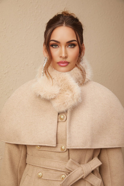 A woman wearing a black faux fur coat with a detachable cape collar standing against a plain background