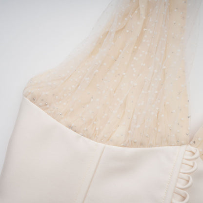 A woman wearing a white halterneck tulle midi dress with a fitted bodice and flowing skirt standing against a plain background