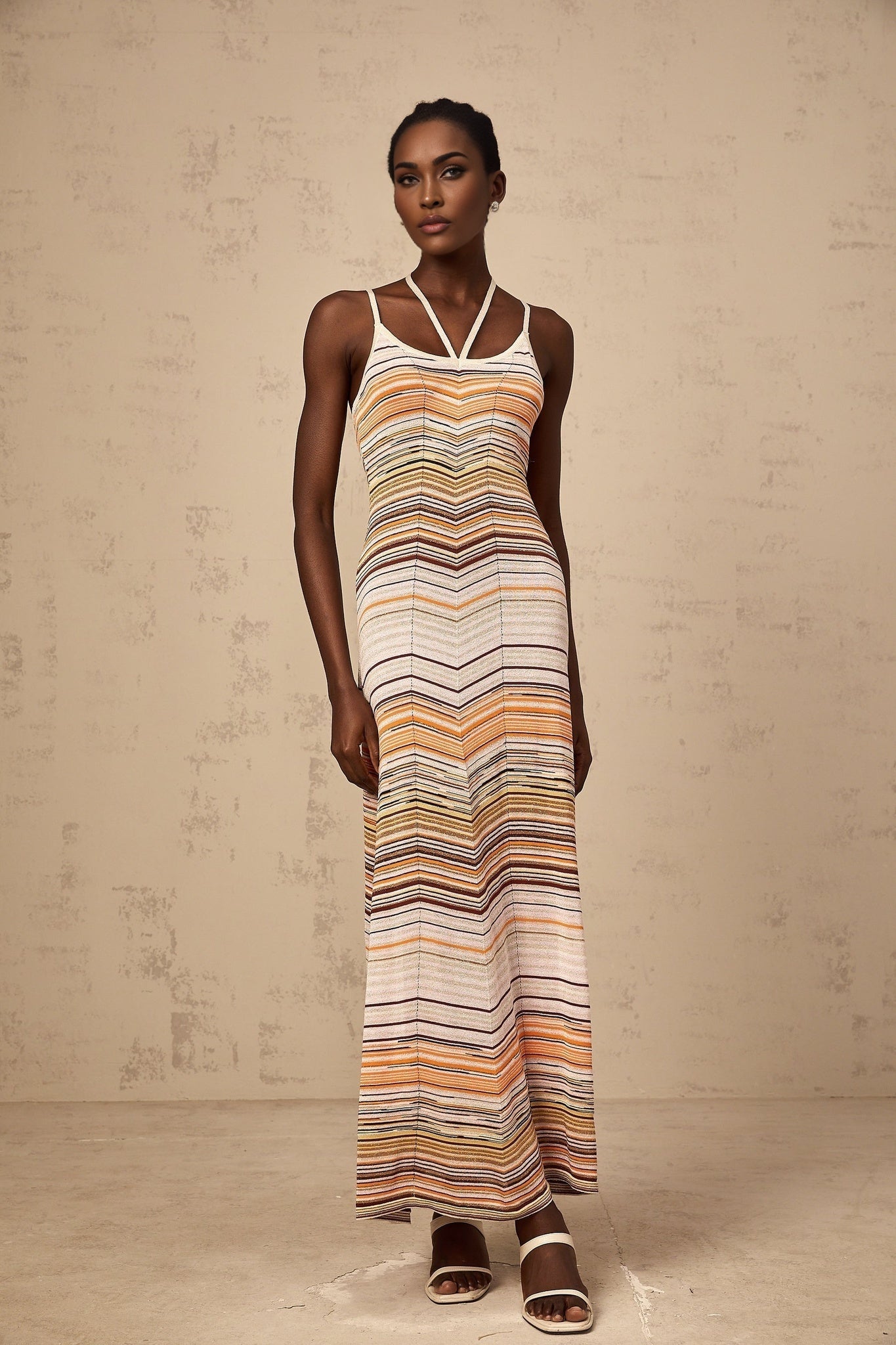 Woman wearing long striped knit maxi dress with multicolored horizontal stripes in pastel shades standing against neutral background