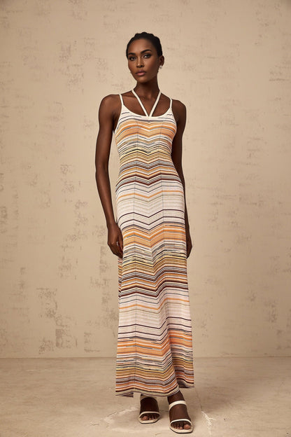 Woman wearing long striped knit maxi dress with multicolored horizontal stripes in pastel shades standing against neutral background