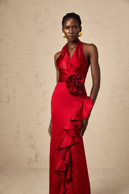 A woman wearing a vibrant red halterneck maxi dress with 3D petal ruffles cascading down the length of the gown creating a dramatic and elegant silhouette