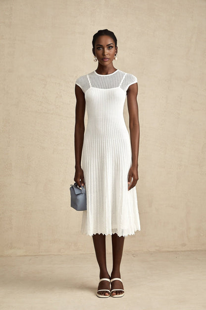 A white semisheer midi dress with scalloped hem details worn by a model standing against a plain background