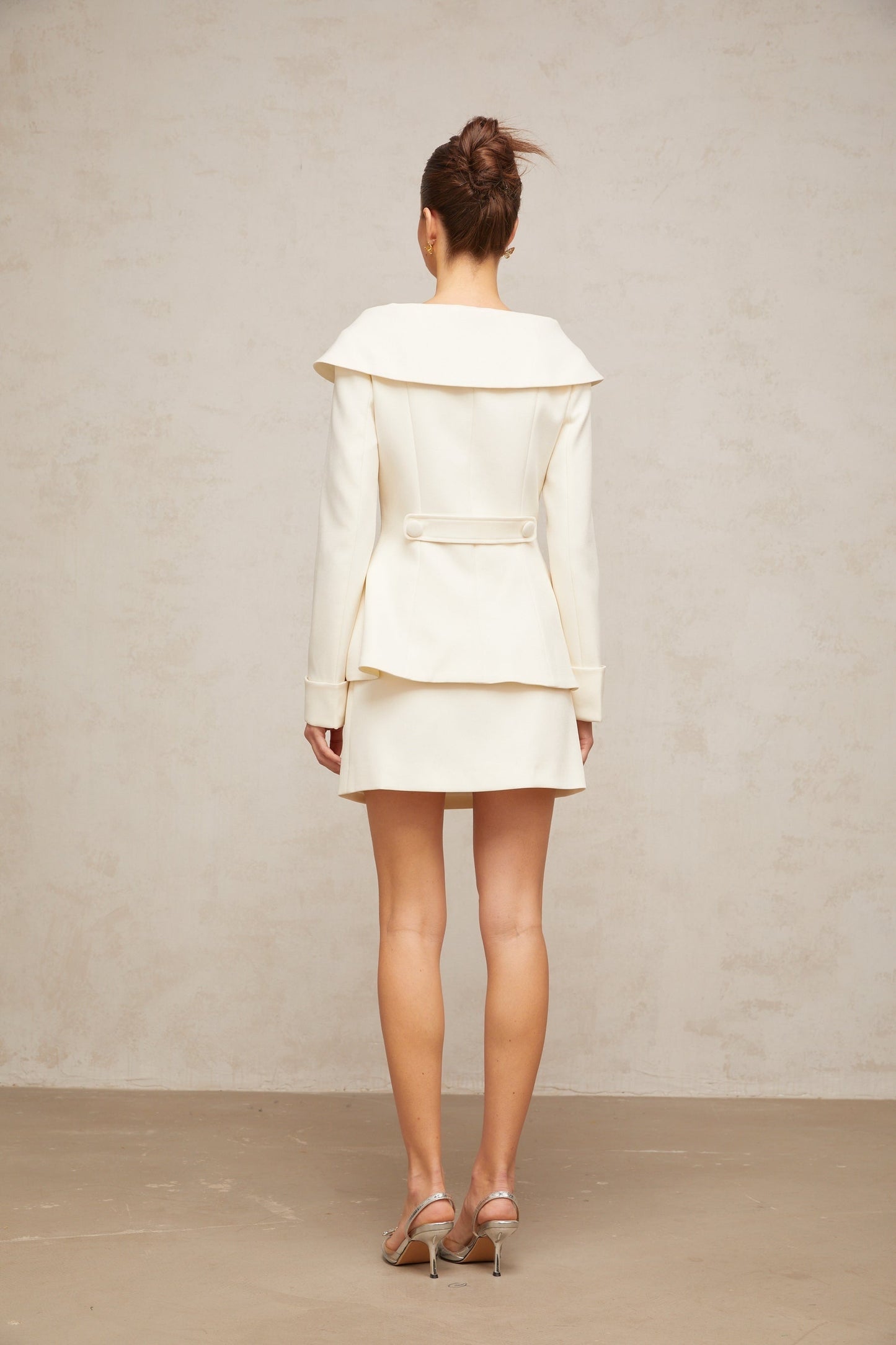 A white peplum jacket paired with a matching skirt creating an elegant two piece ensemble