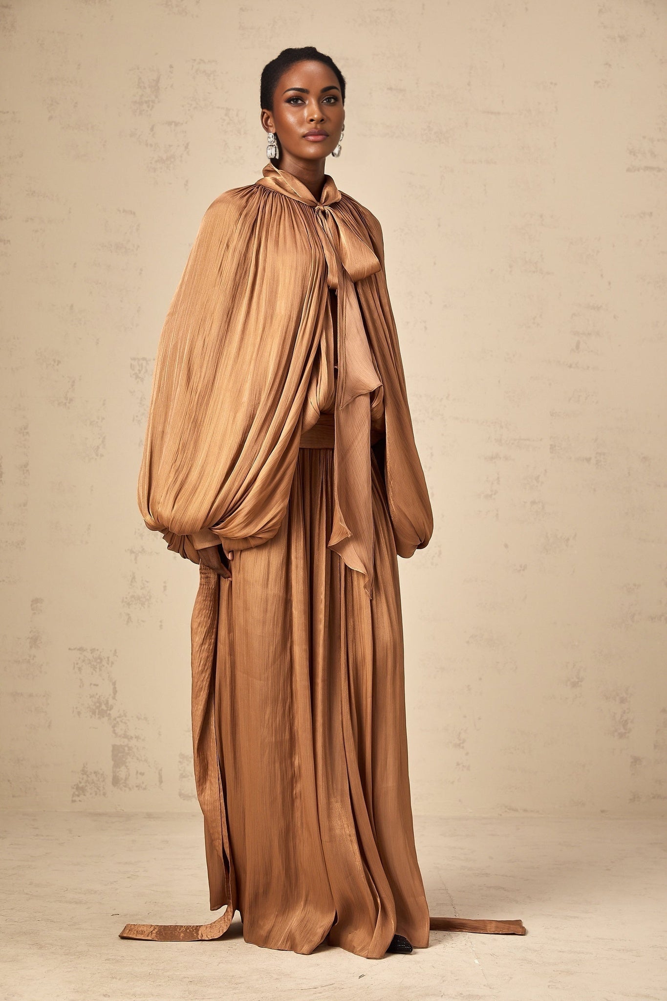 A long brown pleated satin maxi dress with a flowy silhouette and elegant drape
