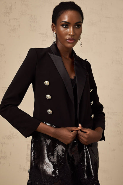 A black cropped blazer with doublebreasted front closure named Giulia worn by a model against a plain background