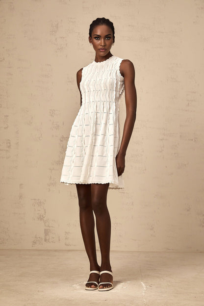 A white sleeveless mini dress with a knit texture and ruffled details worn by a model against a plain background