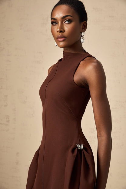 A woman wearing a brown mini dress with an asymmetric neckline and puffed sleeves standing against a plain background
