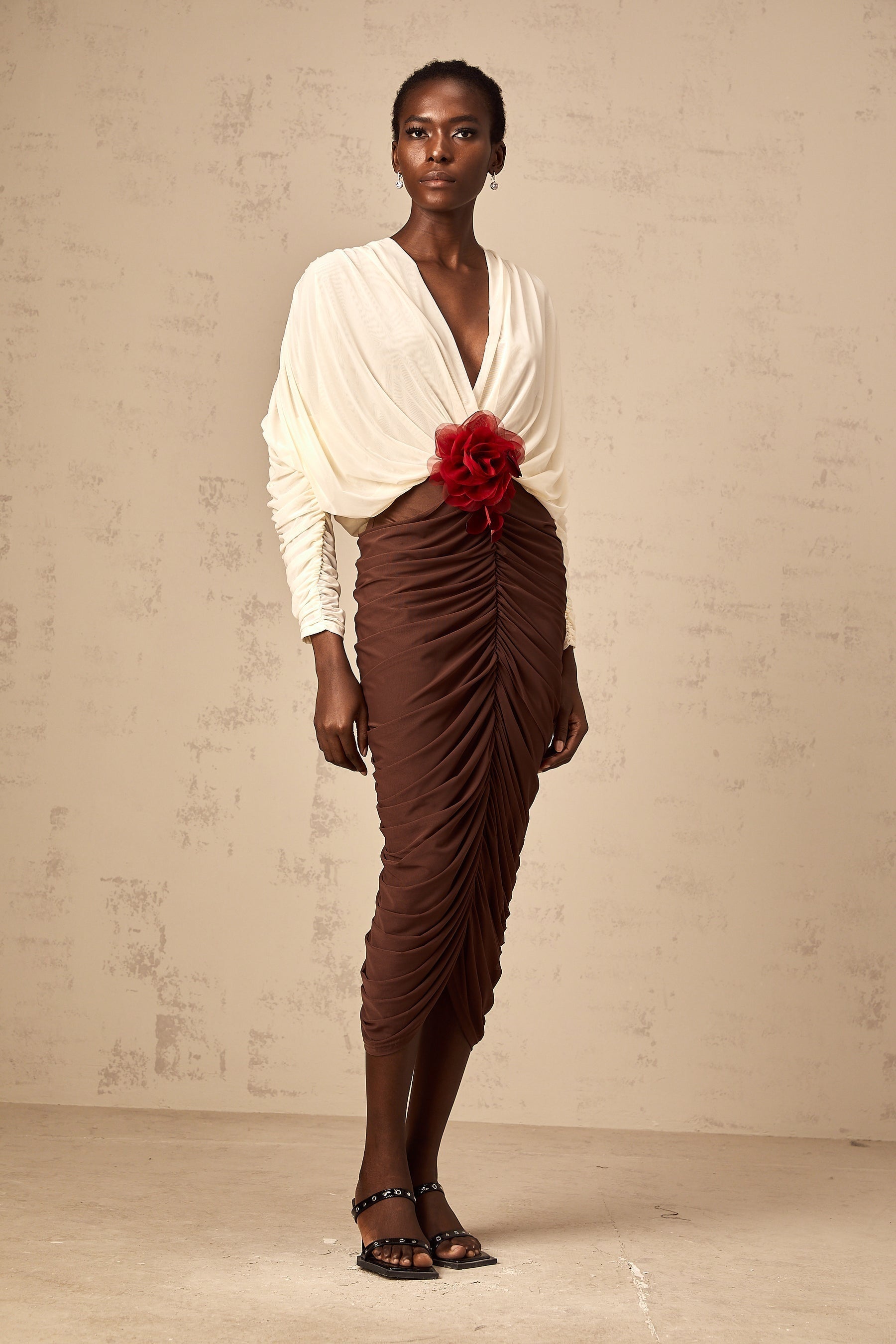 A woman wearing a colorblocked midi dress with ruched detailing and a floral brooch accent The dress features contrasting colors and falls to mid calf length